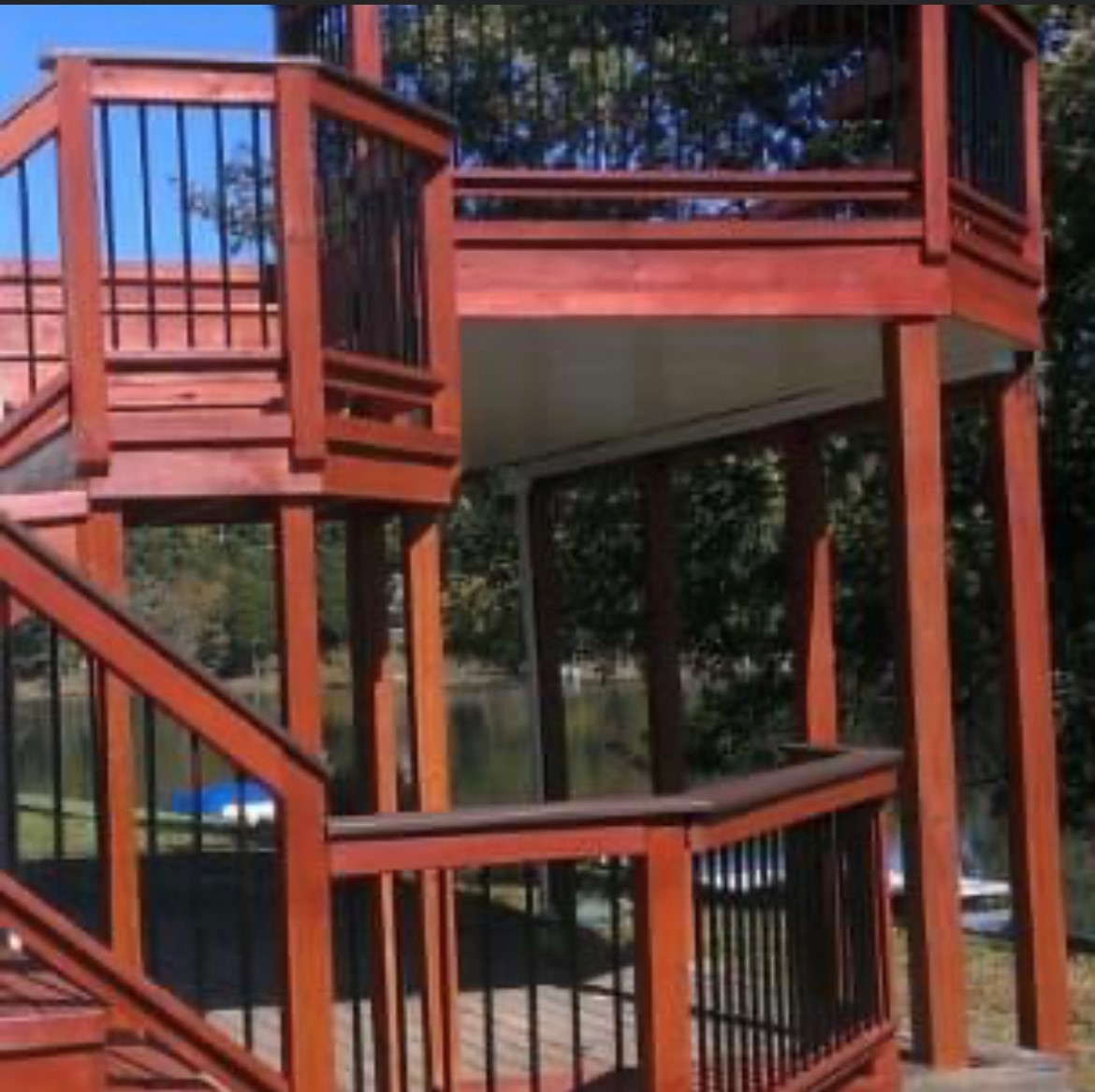Multi-level stained wood deck with black metal railings and staircase, freshly finished in a warm reddish-brown tone