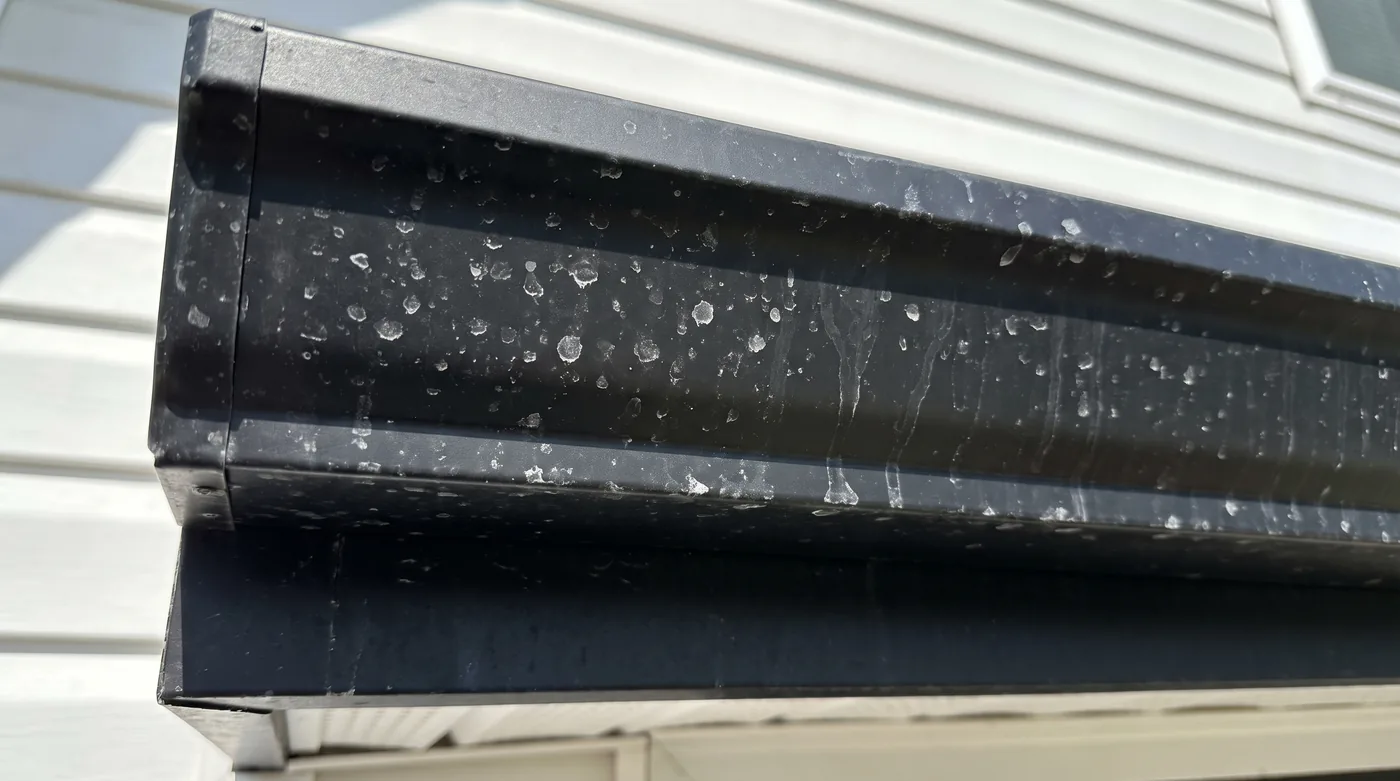 White hard water spots dried on a black aluminum gutter after rinsing